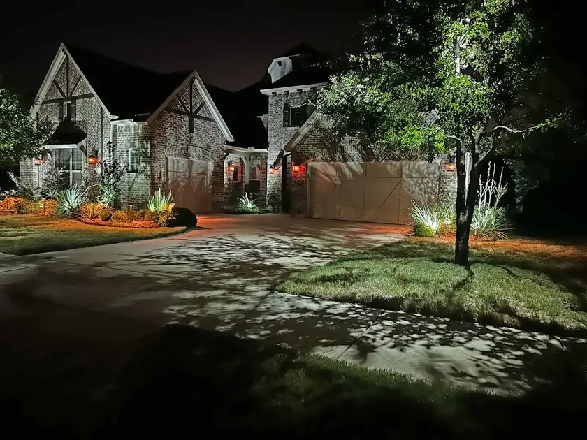 Tudor brick home in Grapevine, Texas with moonlight dappling the driveway and uplit ornamental grasses