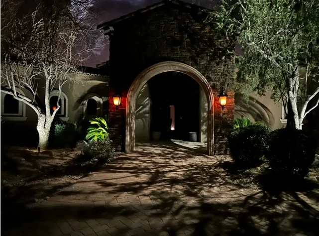 Arched stucco entry in Scottsdale, Arizona washed with warm light, with uplit trees either side of the door