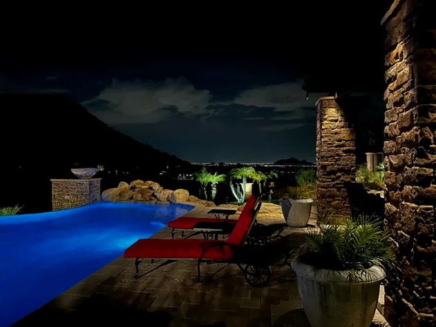 Lit swimming pool glowing blue beside a stone column in Scottsdale, Arizona, with the desert dark beyond