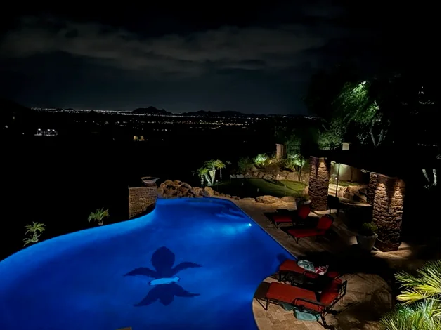 Hillside pool in Scottsdale, Arizona lit at night with uplit palms and the valley lights spread out below