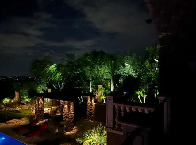 Uplit desert trees around a pool terrace in Scottsdale, Arizona, with a stone wall grazed by warm light