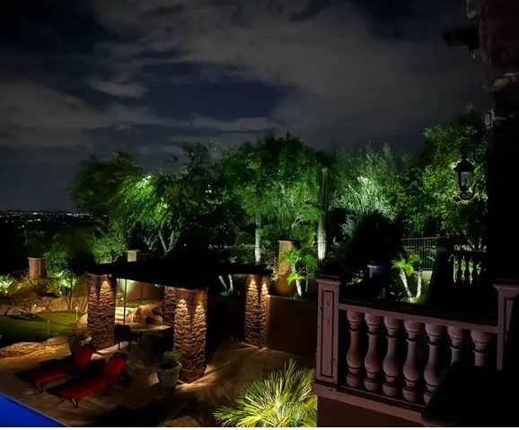 Covered outdoor entertainment area in Scottsdale, Arizona lit after dark, with uplit palms behind the balustrade